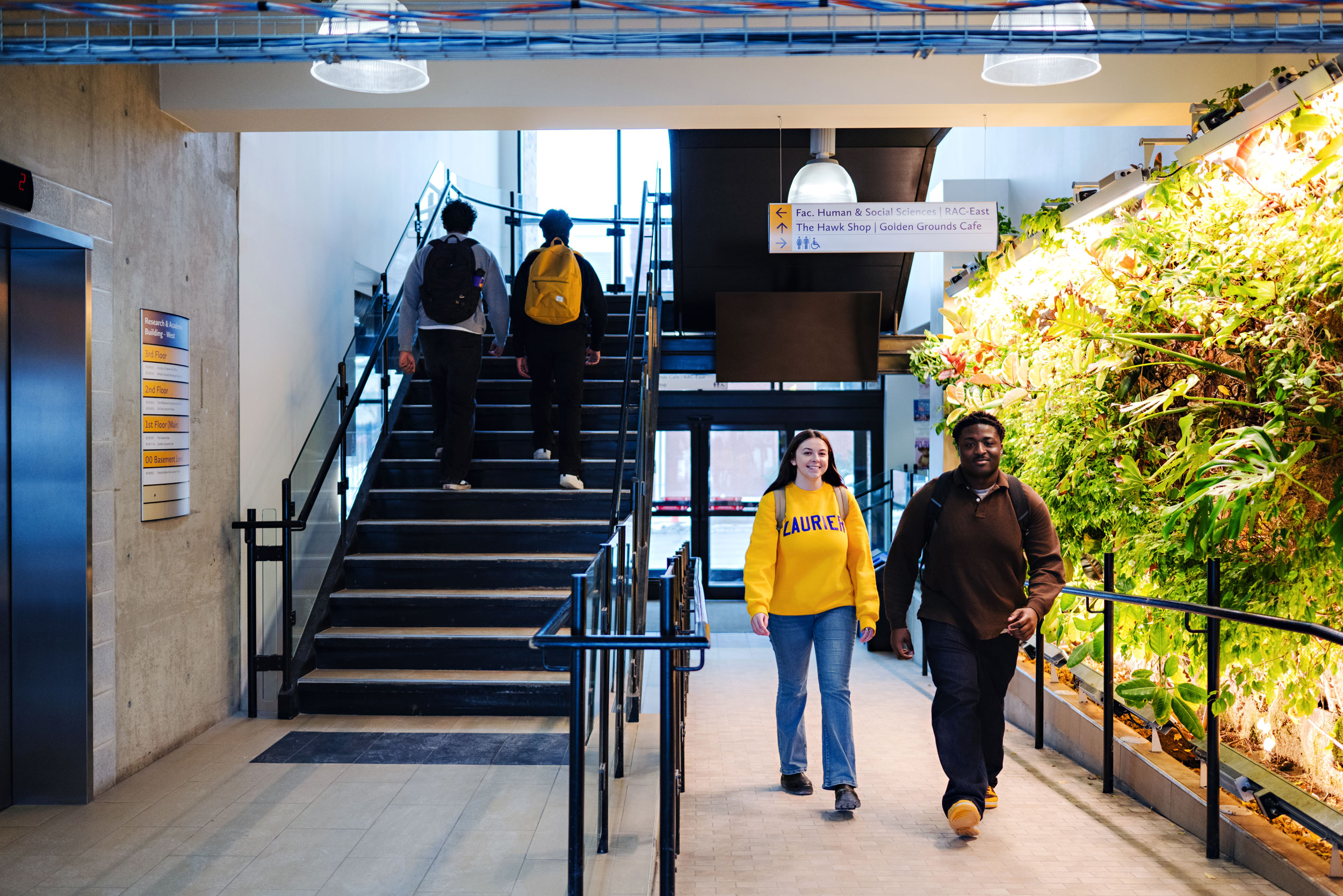 Students walking inside the RAC building with a plant wall on the right