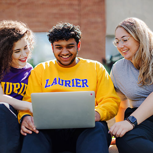 students hang out outside around laptop