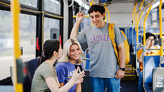 Three students on a city bus looking at a phone