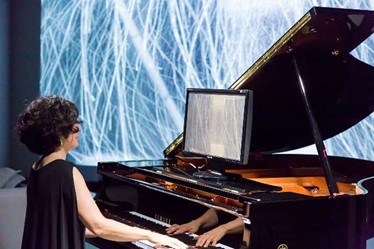 A piano player in the gallery looking at a screen display dynamic graphical representation of the music