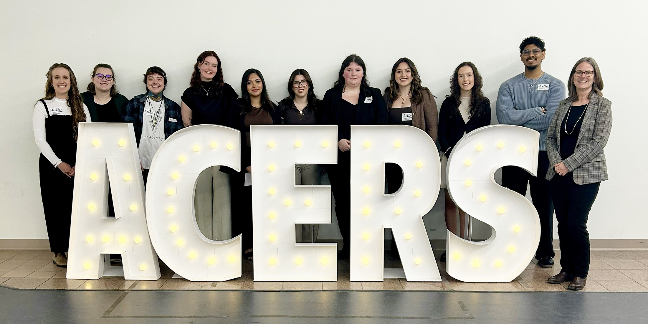 Students and their professor stand in front of an illuminated sign reading ACERS