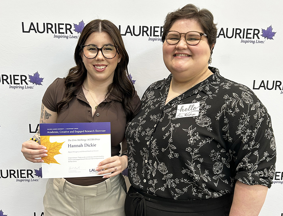 Hannah Dickie and Erin McHarge stand in front of a Laurier-branded backdrop