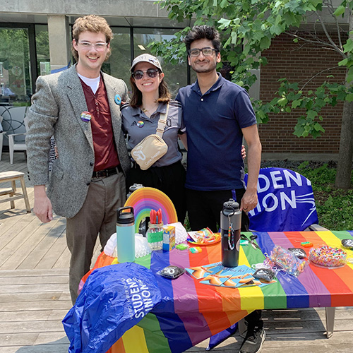Three students standing behind a Pride Month booth