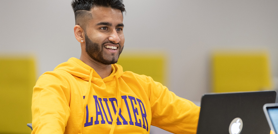 male student smiling wearing yellow Laurier hoodie