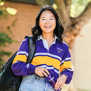 A student smiling at the camera, outdoors during the summer, wearing a Laurier shirt.