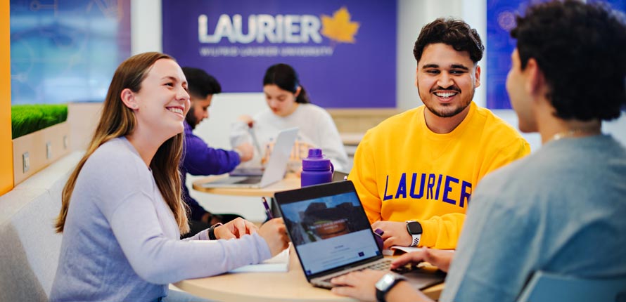 three students smiling sitting at table on milton campus