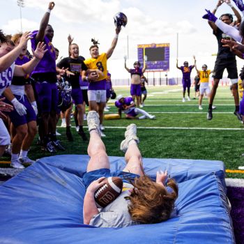 A female falls on a crash mat holding a football.