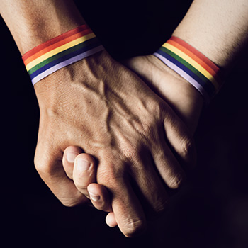 Two people holding hands wearing rainbow bracelets