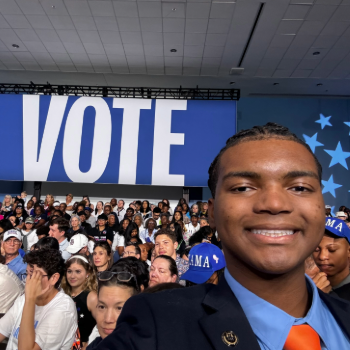 Laurier student Eugene Anekwe poses in front of a large sign that says 'vote'