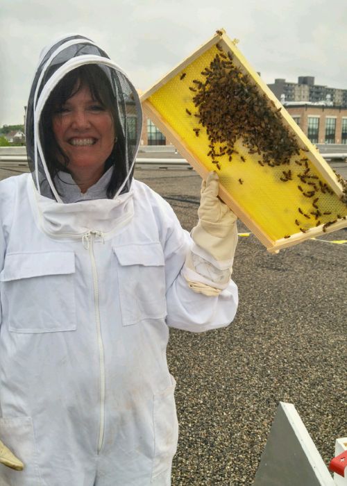 Richelle Monaghan in a beekeeper suit holding bees.