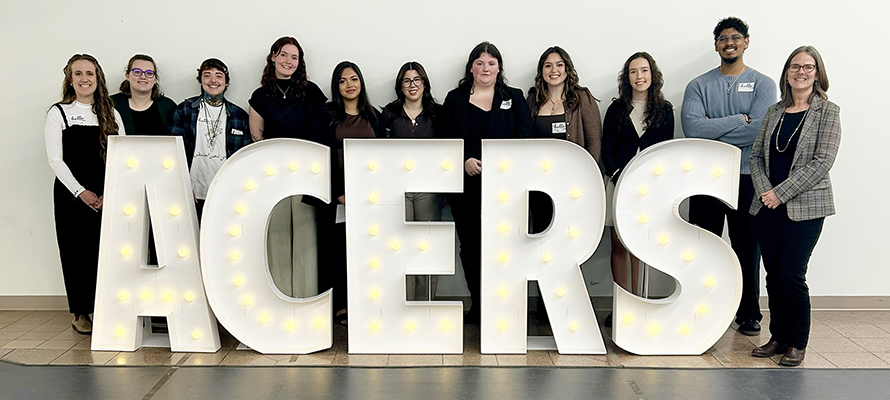 Students and their professor stand behind illuminated sign reading ACERS
