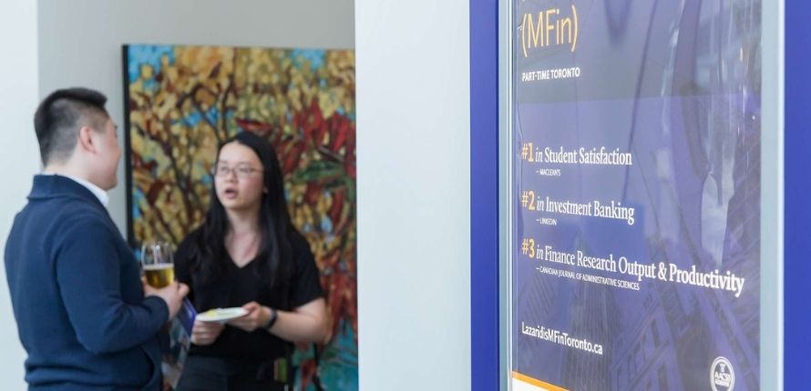 two students talking near an MFin poster